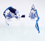 Dois(02) ornamentos de suspensão em faiança esmaltada, decoração em azul e branco à maneira de Delft. Um modelado como anjo músico alado tocando trompa, com motivos florais, asas em relevo e argola metálica para suspensão; outro em forma de árvore alusivo ao pinheiro natalino, apresentando paisagem com moinho. Ambos providos de fitas azuis. Medidas: Alt.: 7 x Comp.: 11,5 x Larg.: 2,5cm; Alt.: 8 x Comp.: 4,5 x Larg.: 1,5 cm