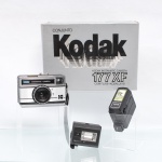 Conjunto fotográfico Kodak Instamatic 177XF. Câmera fotográfica analógica Kodak Instamatic 177XF, para filme em cartucho, corpo retangular em material sintético e metal, objetiva Kodar, visor óptico e seletor de exposição. Acompanha flash Kodak Kodalux 18, unidade de flash National PE-145 e embalagem original do conjunto Kodak. Modelo comercializado em conjunto com o Kodalux 18, conforme referências preservadas do equipamento. Não foi testado, sem garantias de funcionamento.