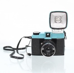 Câmera fotográfica Diana F+ - Lomography. Câmera analógica de médio formato, confeccionada em material sintético nas tonalidades preta e azul-turquesa, destinada a filme 120, com objetiva plástica de 75 mm, foco por zonas, obturador com posições N e B e recursos para múltiplas exposições. Acompanha Diana Flash+, manuais, publicação e acessórios. A Diana F+ constitui reinterpretação contemporânea da câmera Diana difundida a partir da década de 1960. Não foi testada, sem garantias de funcionamento.
