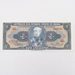 Numismática / Cédulas do Brasil. Cédula de 2 Cruzeiros, República dos Estados Unidos do Brasil, Série 583A, número 053735. Anverso com impressão predominante em tonalidade azul-acinzentada, com efígie do Duque de Caxias em medalhão central, ladeada por rosáceas com o valor facial 2; inscrições Tesouro Nacional, República dos Estados Unidos do Brasil e Dois Cruzeiros  Valor Recebido. Reverso com impressão predominante em tonalidade laranja, apresentando vista aérea da Escola Militar de Resende, atual Academia Militar das Agulhas Negras, ladeada por elementos ornamentais e algarismos indicativos do valor facial. Impressão pela American Bank Note Company. Brasil, década de 1950.