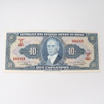 Numismática / Cédulas do Brasil. Cédula de 10 Cruzeiros (Cr$ 10,00), pertencente ao padrão monetário brasileiro do Cruzeiro, emissão do Tesouro Nacional. Estampa 1A, Série 696A, número de ordem 000399, impressa pela American Bank Note Company, Nova York. Anverso com efígie de Getúlio Vargas em medalhão central, ladeada pelo valor facial 10, inscrições República dos Estados Unidos do Brasil, Tesouro Nacional e Dez Cruzeiros  Valor Legal, além das chancelas das autoridades monetárias. Reverso com alegoria da Unidade Nacional, representada por trabalhador manejando ferramenta industrial, tendo instalações fabris ao fundo, ladeada por cartuchos com o valor facial. Impressão calcográfica e tipográfica sobre papel fiduciário. Brasil, 1963.