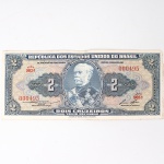 Numismática / Cédulas do Brasil. Cédula de 2 Cruzeiros, República dos Estados Unidos do Brasil, Série 903A, número 000495. Anverso com impressão predominante em tonalidade azul-acinzentada, com efígie do Duque de Caxias em medalhão central, ladeada por rosáceas com o valor facial 2; inscrições Tesouro Nacional, República dos Estados Unidos do Brasil e Dois Cruzeiros  Valor Recebido. Reverso com impressão predominante em tonalidade laranja, apresentando vista aérea da Escola Militar de Resende, atual Academia Militar das Agulhas Negras, ladeada por elementos ornamentais e algarismos indicativos do valor facial. Impressão pela American Bank Note Company. Brasil, década de 1950.