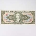 Numismática / Cédulas do Brasil. Cédula de 10 Cruzeiros (Cr$ 10,00), pertencente ao padrão monetário brasileiro do Cruzeiro, emissão do Tesouro Nacional. Estampa 2A, Série 1411A, número de ordem 050714, impressa por Thomas De La Rue & Company Limited, Londres. Anverso com efígie de Getúlio Vargas em medalhão central, ladeada pelo valor facial 10, inscrições República dos Estados Unidos do Brasil, Tesouro Nacional e Dez Cruzeiros  Valor Legal, além das chancelas das autoridades monetárias. Reverso com alegoria da Unidade Nacional, representada por trabalhador manejando ferramenta industrial, tendo instalações fabris ao fundo, ladeada por cartuchos com o valor facial. Impressão calcográfica e tipográfica sobre papel fiduciário. Brasil, década de 1950.