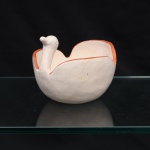 Bowl executado em terracota, representação de ave aquática. Recipiente modelado em corpo semiesférico, com paredes recortadas formando asas laterais e pescoço elevado rematado por cabeça estilizada. Superfície revestida por engobe em tonalidade marfim, com filete alaranjado acompanhando o contorno superior. Olhos indicados por círculos incisos. Interior compartimentado pela própria conformação das paredes. Medidas: Alt.: 11,5 x Comp.: 14 x Larg.: 15 cm.