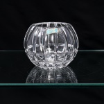 Vaso de centro em cristal ao chumbo, manufatura Violetta, Polônia. Corpo globular, de paredes espessas, com boca circular e perfil segmentado por lapidação manual. A ornamentação organiza-se em gomos verticais facetados na metade superior, sucedidos por faixa de cortes retangulares e quadrangulares dispostos em sequência; porção inferior convergente para o fundo, trabalhada com cortes radiais que formam rosácea vista pela base. Conserva etiqueta de origem com as inscrições "Violetta  Hand Cut  24% Lead Cristal  Made in Poland", identificando cristal com 24% de óxido de chumbo e lapidação manual. Polônia, circa 19701980. Medidas: Alt.: 10 x Diam.: 13 cm.