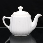 Porcelana Real, Mauá - SP(Fundada em 1943 por Fritz Erwin Schmidt). Bule para chá em porcelana nacional, esmaltagem vítrea na cor branca, corpo bojudo, cilíndrico, aproximadamente cônico, moldado com sucessão de caneluras em relevo, bico vertedor sinuoso de ponta recortada, tampa ligeiramente abualada encimada por pomo de contorno losangular, alça latral estilizada relevada com folhagens acantiformes. Marca da manufatura ao fundo. Medidas: Alt.: 16,5 x Comp.: 23,5 x Larg.: 14 cm.