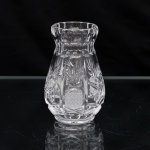 Vaso em cristal europeu, translúcido e incolor, segunda metade do século XX. Corpo de perfil periforme, com base circular e colo estrangulado, rematado por boca de contorno circular. Superfície trabalhada à mão por lapidação, organizada em reservas verticais com motivos de folhagens estilizadas, estrelas e incisões radiais, intercaladas por campos de ponta de diamante. Colo circundado por sequência de facetas ovais e semicirculares. Fundo lapidado em rosácea radial. Conserva etiqueta de origem com a inscrição "Hand Made Crystal  24% PbO", correspondente à composição de cristal ao chumbo com 24% de óxido de chumbo. Manufatura europeia, circa 19601970. Medidas: Alt.: 11 x Diam.: 7 cm.