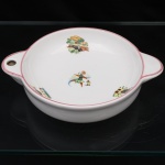 Porcelana Rio Branco / Cia. Brasileira de Vidros, Rio de Janeiro - RJ (fundada em 1947, ativa até 1967). Travessa refratária em porcelana nacional, circa 1950-1960. Corpo circular de paredes baixas, provido de duas pegas laterais integradas, uma delas perfurada para suspensão. Esmaltação branca, bordo e contornos das alças definidos por filetagem rosa. Decoração policroma por decalcomania, distribuída pelo cavado, composta por motivos de hortaliças, legumes, frutos e utensílios de cozinha. Marca da manufatura no verso. Medidas: Alt.: 5 x Comp.: 23,5 x Larg.: 18 cm.