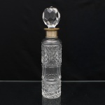 Garrafa decantadora executada em cristal translúcido, datável do período circa 19001930. O exemplar exibe corpo cilíndrico alongado inteiramente decorado por lapidação em padrão bico de jaca de alto relevo nas seções inferior e superior, interrompido por um anel central liso facetado por canaletas verticais.O gargalo recebe guarnição em gola de metal, apresentando punções e numeração "62". Tampa maciça de formato esférico com lapidação poliédrica. Medidas: Alt.: 31 x Diam.: 7cm.