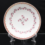 Porcelana Schmidt, Santa Catarina, Brasil (Fundada em 1945). Bowl em porcelana nacional, esmaltação branca, formato hemisférico, decoração composta por grinalda de pequenas rosas em tonalidade rosa, com ramagens e folhagens de tom cinza, circundando arranjo floral disposto no centro. Aba arrematada por faixa contínua em vermelho-vinho, ornamentada com elementos reticulados, volutas e motivos estilizados em douradura. Marca da manufatura no verso. Medidas: Alt.: 6 x Diam.: 25 cm.