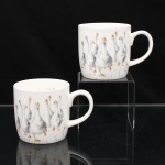 Duas(02) canecas em porcelana inglesa Royal Worcester, coleção Wrendale Designs, padrão "Goosie Goosie", com corpos cilíndricos e alças arqueadas. Decoração estampada segundo ilustrações de Hannah Dale, representando gansos em composição policromada, executada em tonalidades de cinza, branco, preto e ocre, com pontilhados dispersos. Uma das faces apresenta agrupamento de aves e a oposta, figura isolada de ganso. Marca de manufatura no reverso: "Royal Worcester  Established 1751 / Wrendale Designs / Goosie Goosie". Medidas: Alt.: 18 x Comp.: 22,5 x Larg.: 8,5 cm.