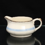 Alfred Meakin, Staffordshire - Inglaterra(Fundada em 1875, ativa até 1976). Molheira em faiança inglesa, Alfred Meakin, Inglaterra, padrão Royal Marigold, circa 1930-40. Corpo bojudo sobre pé anelar, bico vertedor elevado e asa em arco. Esmaltação em tonalidade marfim, ornamentada por faixa horizontal azul-clara percorrida por filete azul. Bordo sinuoso realçado por filetagem  dourado, com douração também aplicada à extremidade da asa. Marca da manufatura Alfred Meakin - England - Royal Marigold. Medidas: Alt.: x Comp.: x Larg.: cm.