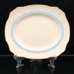 Alfred Meakin, Staffordshire - Inglaterra(Fundada em 1875, ativa até 1976). Travessa oval em faiança inglesa, Alfred Meakin, Inglaterra, padrão Royal Marigold, circa 1930-40. Corpo oval de cavidade rasa, aba larga de contorno ondulado e bordo moldurado. Decoração constituída por faixa perimetral azul-clara, centrada por filete azul, acompanhando o limite interno da aba; realçado por arremate dourado ao longo da orla. Reverso com marca impressa "Alfred Meakin  England  Royal Marigold". Medidas: Comp.: x Larg.: cm.