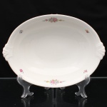Travessa oval em porcelana, manufatura Haas & Czjzek, Horní Slavkov (Schlaggenwald), Tchecoslováquia, circa 1920-1938. Corpo de perfil côncavo, assente sobre pé anelar, com extremidades conformadas por reservas moldadas em relevo. Decoração policroma composta por ramalhetes de rosas e flores miúdas distribuídos pela aba, em tonalidades rosa, azul, amarelo, verde e cinza; contorno realçado por filete dourado. Reverso com marca de fábrica em verde, constituída por coroa, duas árvores estilizadas e monograma, acompanhada da inscrição "Made in Czechoslovakia". Produção atribuída à Haas & Czjzek, manufatura de porcelana da Boêmia cuja denominação empresarial foi estabelecida em 1867 e cuja produção em Horní Slavkov remonta à tradição fabril iniciada no local em 1792. Medidas: Alt.: x Comp.: x Larg.: