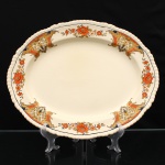 Wood & Sons, Staffordshire - Inglaterra (fundada em 1865/ ativa até 2005). Travessa oval em faiança inglesa, padrão "Woods Ivory Ware", Inglaterra, circa 1930-1940. Corpo de formato oval, aba larga e bordo recortado e moldado com caneluras sucessivas. Decoração por decalcomania policroma, organizada em reservas ornamentais de composição geometrizada e ramalhetes florais, executada em tons de laranja, ocre, preto e creme; contorno interno definido por filete preto. Reverso com marca de fábrica "Woods Ivory Ware  England", encimada por coroa. A linha Woods Ivory Ware foi introduzida pela Wood & Sons por volta de 1930. Medidas: Comp.: x Larg.: cm.