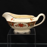 Wood & Sons, Staffordshire - Inglaterra (fundada em 1865 / ativa até 2005). Molheira em faiança fina inglesa, parão "Woods Ivory Ware", Inglaterra, circa 1930-1940. Corpo de perfil bojudo, bico vertedor alongado, alça lateral arqueada e pé moldado de contorno ondulado. Decoração por decalcomania policroma constituída por ramalhetes florais alternados com cartelas ornamentais de desenho geometrizado, em laranja, ocre, preto e creme; pequenos motivos florais complementam a composição junto ao bordo, filetes pretos percorrem a embocadura, a alça e o pé. Reverso com marca "Woods Ivory Ware  England", encimada por coroa. Medidas: Alt.: 7,5 x Comp.: 7,5 x Larg.: 12cm.