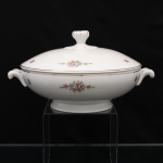 Sopeira em porcelana, provavelmente de manufatura europeia, circa 1930-1950. Corpo ovalado e bojo profundo, elevado sobre pé anelar, guarnecido por alças laterais moldadas em volutas, realçadas por filetes dourados. Tampa abaulada com pomo canelado de configuração floral, circundado por elementos moldados em relevo. Esmaltação branca, dotada de decoração policroma composta por buquês e pequenos ramos de flores, com rosas em tonalidades de rosa, cinza, amarelo e azul, acompanhadas de folhagem verde, filetação a ouro acompanha o bordo da tampa, do bojo, detalhes das alças e do pomo. Sem marca de manufatura. Datação atribuída pelas características formais e ornamentais. Medidas: Alt.: 14 x Comp.: 27 x Larg.: 21,5 cm.
