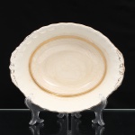 W.H. GRINDLEY, Staffordshire - Inglaterra(Fundada por William Harry Grindley em 1880). Travessa funda em faiança inglesa, padrão "CREAMPETAL", c.1940-50. Esmaltagem vítrea de tonalidade marfim claro, formato oval de interior côncavo, orla modelada com faixa perimetral ondulada, percorrida por perolados relevados na própria pasta, ornamentada por filetagem à ouro contornando a borda e a caldeira, abas laterais integradas e decoradas com ramagens. Apresenta ínfimos degastes de uso na douradura, e leves manchas do tempo. Marca da manufatura no verso. Medidas: Alt.: 7 x Comp.: 26 x Larg.: 20 cm.