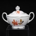 Porzellanfabrik Zeh, Scherzer & Co, Baviera - Alemanha (Fundada em 1880). Excepcional açucareiro em porcelana alemã da década de 1930, estilo e período Art Déco. Esmaltagem vítrea na cor branca, dotada de decoração em estampagem policromada, com flores e ramagens outonais nas tonalidades coral, ocre, azul e amarelo, realçada por filetação prateada nas bordas e detalhes. Bojo hemisférico assentado sobre base cirular elevada de borda recortada, asas laterais em voluta, tampa ligeiramente abaulada encimada por puxador com feitio de fruto. Borda lateral possui contorno relevado com sucessão de frisos radias interrompidos por folha de acanto estilizada. Marca da manufatura ao fundo, acompanhada de selo comemorativo de 50 anos de fundação da marca com a inscrição "50 JAHRE"(O timbre "50 Jahre" (50 anos) identifica a tiragem limitada produzida pela Porzellanfabrik Zeh, Scherzer & Co. AG de forma exclusiva no decorrer do ano de 1930, em celebração ao cinquentenário de fundação da fábrica em Rehau, na Baviera). Medidas: Alt.: 11 x Comp.: 16,5 x Larg.: 12 cm.
