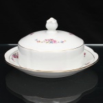 CHODZIEZ PORCELAIN, Chodziez - Polônia(Fundada em 1852 ou 1854, por Hermann Müller e Ludwik Schnorr). Manteigueira em porcelana polonesa da década de 1940; esmaltagem vítrea na cor branca, tampa circular de topo abaulado, encimado por pomo com feitio de fruto, prato dotado de receptáculo cilíndrico central integrado. Decorada com padrão floral em estampagem policromada, composto de arranjo floral nas tonalidades rosa, azul, amarelo e verde, e buquês distribuídos na orla do prato e no topo da tampa, bordo circundado por barrado contínuo relevado na própria pasta. Apresenta filetagem à ouro nas bordas e detalhes. Marca da manufatura no verso. Medidas: Alt.: 9,5 x Diam.: 18 cm.