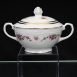 CHODZIEZ PORCELAIN, Chodziez - Polônia(Fundada em 1852 ou 1854, por Hermann Müller e Ludwik Schnorr). Açucareiro em porcelana polonesa da década de 1940; esmaltagem vítrea na cor branca, corpo bojudo de formato hemisférico assentado sobre base circular recortada, alças lateras em voluta, tampa abaulada encimada por pomo com feitio de fruto; decorada com padrão floral em estampagem policromada, composto de arranjo floral nas tonalidades rosa, azul, amarelo e verde, e buquês distribuídos no terço superior do bojo sob barrado contínuo relevado na própria pasta. Apresenta filetagem à ouro nas bordas e detalhes. Marca da manufatura no verso. Medidas: Alt.: 10 x Comp.: 15,5 x Larg.: 11 cm.