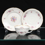CHODZIEZ PORCELAIN, Chodziez - Polônia(Fundada em 1852 ou 1854, por Hermann Müller e Ludwik Schnorr). Belíssimo trio para chá em porcelana polonesa da década de 1940; esmaltagem vítrea na cor branca, bojo hemisférico assentado sobre base circular recortada, alça lateral em voluta; decorada com padrão floral em estampagem policromada, composto de arranjo floral nas tonalidades rosa, azul, amarelo e verde, e buquês distribuídos nas orlas do pires e do prato. Apresenta filetagem à ouro nas bordas interna e externa. Orla delimitada por barrado contínuo relevado na própria pasta. Padrão decorativo integralmente replicado no pires e no prato. Marca da manufatura no verso. Medidas: Xícara: Alt.: 5 x Comp.: 12 x Larg.: 10 cm; Prato: Diam.: 17 cm; Pires: Diam.: 15 cm.