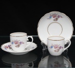 Porcelana Real, Mauá - SP(Fundada em 1943 por Fritz Erwin Schmidt). Duas(02) xícaras para café em porcelana de fabricação nacional, circa 1960-1970. Esmaltagem vítrea na cor branca, bojo oval, asa lateral escultural em formato de voluta com terminação em rolo superior, ornamentação com motivos pictóricos policromados por processo de decalcomania fina inspirados no estilo "Deutsche Blumen", completado com filetagem à ouro nas bordas e margens. Padrão decorativo replicado no pires em reservas na orla, aba percorrida por gomos ondulares suaves. Marca da manufatura no verso. Medidas: Xícara: Medidas: Alt.: 5 x Comp.: 6,5 x Larg.: 5 cm; Pires: Diam.: 10,5 cm.