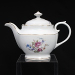 Porcelana Real, Mauá - SP(Fundada em 1943 por Fritz Erwin Schmidt). Belíssimo bule para chá executado em porcelana nacional, circa 1960-1970. Bojo oval alargado assente sobre base circular, tampa abaulada encimada por puxador aproximadamente cônico, bico vertdor curvado de ponta recortada e asa lateral em voluta. Esmaltagem vítrea na cor branca, ornamentação com motivos pictóricos policromados por processo de decalcomania fina inspirados no estilo "Deutsche Blumen", distribuídos pelo bojo e no topo da tampa, realçada por filetagem à ouro nas bordas e margens. Marca da manufatura ao fundo. Medidas: Alt.: 16 x Comp.: 22,5 x Larg.: 13,5 cm.