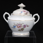 Porcelana Real, Mauá - SP(Fundada em 1943 por Fritz Erwin Schmidt). Belíssima açucareiro executado em porcelana nacional, ao estilo francês do período Luís XV, circa 1960-1970. Bojo hemisférico assente sobre base circular, tampa abobadada encimada por puxador aproximadamente cônico facetado com seis lados, alças laterais em volutas. Esmaltagem vítrea na cor branca, ornamentação com motivos pictóricos policromados por processo de decalcomania fina inspirados no estilo "Deutsche Blumen", distribuídos pelo bojo e pelo topo da tampa, realçada por filetagem à ouro nas bordas e margens. Marca da manufatura ao fundo. Medidas: Alt.: 11,5 x Comp.: 13,5 x Larg.: 10 cm.