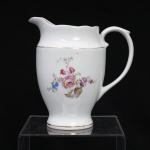 Porcelana Real, Mauá - SP(Fundada em 1943 por Fritz Erwin Schmidt). Belíssima leiteira executada em porcelana nacional, circa 1960-1970. Bojo oval alargado assente sobre base circular, bico vertedor revirado para fora, borda recortada e asa lateral em voluta. Esmaltagem vítrea na cor branca, ornamentação com motivos pictóricos policromados por processo de decalcomania fina inspirados no estilo "Deutsche Blumen", realçada por filetagem à ouro nas bordas e margens. Marca da manufatura ao fundo. Medidas: Alt.: 14 x Comp.: 14 x Larg.: 9 cm.