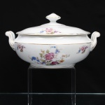 Porcelana Real, Mauá - SP(Fundada em 1943 por Fritz Erwin Schmidt). Belíssima terrina coberta, para vegetais, executada em porcelana nacional, circa 1960-1970. Bojo hemisférico, tampa ligeiramente abaulada encimada por puxador aproximadamente cônico facetado, alças laterais reviradas terminadas em voolutas. Esmaltagem vítrea na cor branca, ornamentação com motivos pictóricos policromados por processo de decalcomania fina inspirados no estilo "Deutsche Blumen", distribuídos pelo bojo e pelo topo da tampa, realçada por filetagem à ouro nas bordas e margens. Marca da manufatura ao fundo. Medidas: Alt. 15,5 x Comp.: 27 x Larg.:  23 cm.