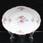 Porcelana Real, Mauá - SP(Fundada em 1943 por Fritz Erwin Schmidt). Belíssima travessa oval executada em porcelana nacional, circa 1960-1970. Esmaltagem vítrea na cor branca, ornamentação com motivos pictóricos policromados por processo de decalcomania fina inspirados no estilo "Deutsche Blumen", replicado nas reservas periféricas da orla, aba percorrida por gomos ondulares suaves, realçado com filetagem à ouro nas bordas e margens. Marca da manufatura no verso. Medidas: Comp.: x Larg.: cm.