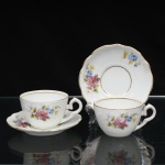 Porcelana Schmidt, Santa Catarina, Brasil (Fundada em 1945). Duas(02) xícaras para café em porcelana nacional, c.1950/60, executado com elementos derivados do repertório Luís XV. Bojo hemisférico, alça lateral em voluta, borda do pires recortada em suave ondulações. Esmaltagem vítrea na cor branca, decoração floral policroma aplicada por decalcomania, constituída por ramagens e corolas em rosa, azul, amarelo e folhagens verde, complementada por filetagem em dourada nas bordas, base e alça. Marca da manufatura ao fundo. Medidas xícara: Alt.: 5 x Comp.: 11 x Larg.: 8,5 cm.; Pires: Diam.: 13,5 cm; Prato: Diam.: 16,5 cm.