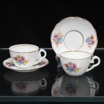 Porcelana Schmidt, Santa Catarina, Brasil (Fundada em 1945). Duas(02) xícaras para café em porcelana nacional, c.1950/60, executado com elementos derivados do repertório Luís XV. Bojo hemisférico, alça lateral em voluta, borda do pires recortada em suave ondulações. Esmaltagem vítrea na cor branca, decoração floral policroma aplicada por decalcomania, constituída por ramagens e corolas em rosa, azul, amarelo e folhagens verde, complementada por filetagem em dourada nas bordas, base e alça. Marca da manufatura ao fundo. Medidas xícara: Alt.: 5 x Comp.: 11 x Larg.: 8,5 cm.; Pires: Diam.: 13,5 cm; Prato: Diam.: 16,5 cm.