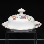 Porcelana Schmidt, Santa Catarina, Brasil (Fundada em 1945). Belíssima manteigueira executada em porcelana nacional, circa 1950/60. Tampa em cúpula abobadada encimada por pomo facetado com seis lados, prato dotado de receptáculo cilíndrico central integrado, borda recortada, realçada por filetagem à ouro nas bordas e margens. Decoração floral policroma aplicada por decalcomania, constituída por ramagens e corolas em rosa, azul, vermelho, amarelo e folhagens verde. Marca da manufatura ao fundo. Medidas: Alt.: 8 x Diam.: 15 cm.