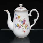 Porcelana Schmidt, Santa Catarina, Brasil (Fundada em 1945). Bule para café em porcelana nacional, c.1950/60, executado com elementos derivados do repertório Luís XV. Bojo oval alongado, borda recortada e ligeiramente revirada para fora, tampa abaulada encimada por puxador facetado, bico vertedor cuervilíneo, asa lateral em voluta. Esmaltagem vítrea na cor branca, decoração floral policroma por decalcomania, constituída por ramagens e corolas em rosa, azul, vermelho, amarelo e folhagens verde, complementada por filetagem em dourada na base, tampa, pomo, alça e extremidade do bico. Marca da manufatura ao fundo. Medidas: Alt.: 21,5 x Comp.: 23 x Larg.: 11 cm.