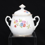 Porcelana Schmidt, Santa Catarina, Brasil (Fundada em 1945). Bule para chá em porcelana nacional, c.1950/60, executado com elementos derivados do repertório Luís XV. Corpo bojudo, borda recortada e ligeiramente revirada para fora, tampa abaulada encimada por puxador facetado, asas laterais em voluta. Esmaltagem vítrea na cor branca, decoração floral policroma por decalcomania, constituída por ramagens e corolas em rosa, azul, vermelho, amarelo e folhagens verde, complementada por filetagem em dourada na base, tampa, pomo e alças laterais. Marca da manufatura ao fundo. Medidas: Alt.: 12,5 x Comp.: 14,5 x Larg.: 10 cm.