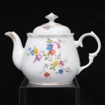 Porcelana Schmidt, Santa Catarina, Brasil (Fundada em 1945). Bule para chá em porcelana nacional, c.1950/60, executado com elementos derivados do repertório Luís XV. Corpo bojudo, borda recortada e ligeiramente revirada para fora, tampa abaulada encimada por puxador facetado, bico vertedor curvilíneo, asa lateral em voluta. Esmaltagem vítrea na cor branca, decoração floral policroma por decalcomania, constituída por ramagens e corolas em rosa, azul, vermelho, amarelo e folhagens verde, complementada por filetagem em dourada na base, tampa, pomo, alça e extremidade do bico. Marca da manufatura ao fundo. Medidas: Alt.: 16 x Comp.: 22,5 x Larg.: 13,5 cm.