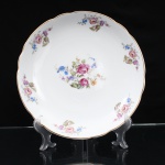 Porcelana Real, Mauá - SP(Fundada em 1943 por Fritz Erwin Schmidt). Belíssima travessa circular executada em porcelana nacional, circa 1960-1970. Esmaltagem vítrea na cor branca, centro ornamentado com motivos pictóricos policromados por processo de decalcomania fina inspirados no estilo "Deutsche Blumen", replicado nas reservas periféricas que circundam a orla, aba percorrida por gomos ondulares suaves, realçado com filetagem à ouro na borda. Marca da manufatura no verso. Medidas: Diam.: 26 cm.