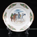 Prato de serviço em porcelana nacional, manufatura Emano, com duas pegas laterais e filete dourado no bordo. Reserva central com reprodução em estampagem policromada da obra "Campagne de France", 1814, de Jean-Louis-Ernest Meissonier (1815-1891), representando Napoleão I a cavalo, trajando bicorne e redingote, seguido por oficiais de seu estado-maior montados, em episódio da campanha militar de 1814. A cena representa o avanço das forças da Sexta Coalizão sobre território francês. O imperador é figurado a cavalo, acompanhado por oficiais e integrantes de seu estado-maior, durante o deslocamento em direção a Soissons após a Batalha de Laon, travada em março daquele ano. A inscrição Meissonier, aposta junto à composição, identifica a referência iconográfica empregada na decoração. Aba ornamentada por cartelas simétricas de inspiração neorrococó, constituídas por volutas em bege e castanho, campos reticulados em verde e medalhões com motivos fitomórficos. Pegas moldadas e douradas. No reverso, etiqueta da manufatura "EMAN0 - Ind. Bras.". Brasil, século XX. Medida: Diam.: