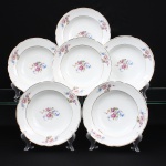 Porcelana Real, Mauá - SP (Fundada em 1943 por Fritz Erwin Schmidt). Conjunto de pratos fundos em porcelana de pasta dura, fabricação nacional, circa 1960-1970. Esmaltagem vítrea na cor branca, centro dotado de ornamentação com motivos pictóricos policromados por processo de decalcomania fina inspirados no estilo Deutsche Blumen, completado com filetagem à ouro na borda e ao redor da caldeira, reservas na orla retratam um buquê clássico composto por rosa púrpura centralizada, violetas, miosótis e folhagens detalhadas em tons esmeralda, aba percorrida por gomos ondulares suaves. Marca da manufatura no verso. Composto de seis(06) unidades. Medida: Diam.: 24 cm.
