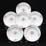 Porcelana Real, Mauá - SP (Fundada em 1943 por Fritz Erwin Schmidt). Conjunto de pratos fundos em porcelana de pasta dura, fabricação nacional, circa 1960-1970. Esmaltagem vítrea na cor branca, centro dotado de ornamentação com motivos pictóricos policromados por processo de decalcomania fina inspirados no estilo Deutsche Blumen, completado com filetagem à ouro na borda e ao redor da caldeira, reservas na orla retratam um buquê clássico composto por rosa púrpura centralizada, violetas, miosótis e folhagens detalhadas em tons esmeralda, aba percorrida por gomos ondulares suaves. Marca da manufatura no verso. Composto de seis(06) unidades. Medida: Diam.: 24 cm.