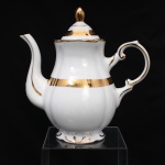 Porcelana Rio Branco / Cia. Brasileira de Vidros, Rio de Janeiro - RJ (fundada em 1947, ativa até 1967). Bule para café em porcelana nacional da década de 1950-60, executado ao estilo francês do período Luís XV. Bojo piriforme moldado com gomos em relevo, borda reocortada em arcos, tampa campaniforme encimada por pomo ovoide, bico vertedor curvilíneo, asa alta em forma de voluta. em porcelana nacional. Esmaltagem vítrea na cor branca, com bordos de perfil ondulado, ornamentação constituída por faixa dourada com friso de ramagens florais estilizadas, complementada por filetes a ouro no bordo, alça e na tampa. Marca da mnanufatura ao fundo. Medidas: Alt.: x Comp.: x Larg.: cm.