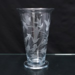 Vaso executado em cristal incolor, corpo obcônico com bordo evertido, assente sobre base circular. Superfície ornamentada por gravação fosca de composição fitomórfica, formada por hastes, folhas lanceoladas, botões e flores estilizadas distribuídas pelo bojo.  Medidas: Alt.: 22 x Diam.: 14 cm. Apresenta bicados na borda, vide foto.