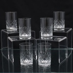 Conjunto de copos executados em meio cristal, diáfano e incolor, formato cilíndrico de base espessa, talhado com faixa geométrica composta por losangos facetados e cortes diagonais entrecruzados na porção inferior. Composto de seis(06) unidades. Medidas. Altura  x Diâmetro:  cm.