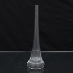 Vaso solitário em cristal incolor, de corpo alongado e perfil cônico, estreitando-se progressivamente em direção ao colo e terminando em boca de seção quadrangular. Fuste facetado por arestas longitudinais, assentado sobre base circular espessa, de contorno convexo e fundo rebaixado. Peça executada em cristal maciço na região inferior, com transição contínua entre base e haste. Medidas: Alt.: x Diam.: