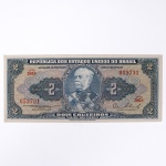 Numismática / Cédulas do Brasil. Cédula de 2 Cruzeiros, República dos Estados Unidos do Brasil, Série 583A, número 053731. Anverso com impressão predominante em tonalidade azul-acinzentada, com efígie do Duque de Caxias em medalhão central, ladeada por rosáceas com o valor facial 2; inscrições Tesouro Nacional, República dos Estados Unidos do Brasil e Dois Cruzeiros  Valor Recebido. Reverso com impressão predominante em tonalidade laranja, apresentando vista aérea da Escola Militar de Resende, atual Academia Militar das Agulhas Negras, ladeada por elementos ornamentais e algarismos indicativos do valor facial. Impressão pela American Bank Note Company. Brasil, década de 1950.