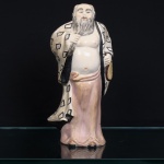 Escultura chinesa executada em porcelana moldada e esmaltada, representando Zhongli Quan, um dos Oito Imortais da tradição taoista. Figura masculina de ventre exposto, barba longa e calvície, trajando túnica em tom marfim com contornos pretos e motivos geométricos, sobre veste inferior em tom rosado. Na mão esquerda, segura leque de formato oval, atributo iconográfico associado a Zhongli Quan. Policromia em tons de marfim, rosa, cinza, preto, amarelo e marrom. Marca em vermelho sob a base. Medidas: Alt.: 29 x Comp.:13 x Larg.: 10cm.