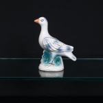 Escultura animalista executada em cerâmica esmaltada, representando pássaro em posição ereta, modelado sobre base integrada com relevos alusivos à vegetação aquática. Plumagem em branco com sombreados azulados, detalhes lineares metalizados, bico em tonalidade alaranjada e elementos da sustentação em azul-turquesa. Base oval com marca numérica em relevo 68 e abertura central de queima. .Medidas: Alt.: 18 x Comp.: 19,5 x Larg.: 8cm