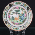 Prato executado em porcelana chinesa, decoração policromada e dourada executada em esmaltes sobre o vidrado, ao gosto da Família Rosa. Reserva central delimitada por cartela lobulada, contendo composição com tigre e ave de rapina, entre pinheiro, formações rochosas, flores e vegetação. Aba ornamentada por painéis alternados com frutos e motivos florais, intercalados por medalhões circulares contendo caracteres auspiciosos, além de frisos geométricos em vermelho-ferro e negro. Contorno realçado por filete alaranjado. No reverso, marca quadrangular em vermelho-ferro com quatro caracteres chineses(Huali Chang Zao). Medida: Diam.: 21cm.